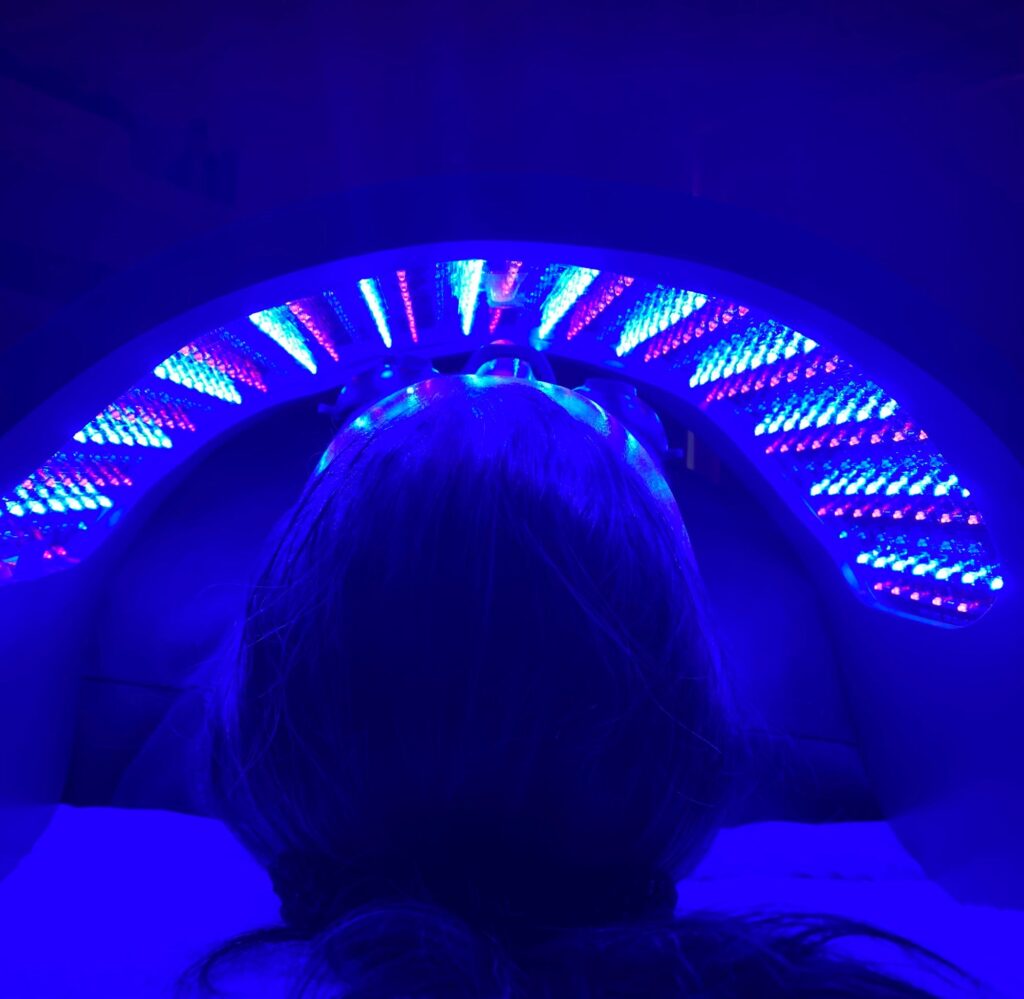 A patient laying under the light device used for Celluma light therapy in Westlake, OH. The device is set to the blue light setting.